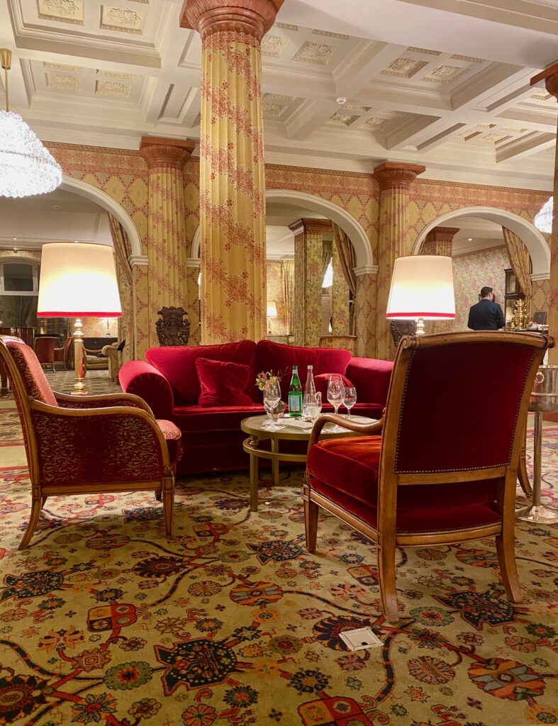 Hotel Kulm, St. Moritz, large fireplace mantel, gold and ruby wallpaper, gold and ruby upholstery, red velvet furniture